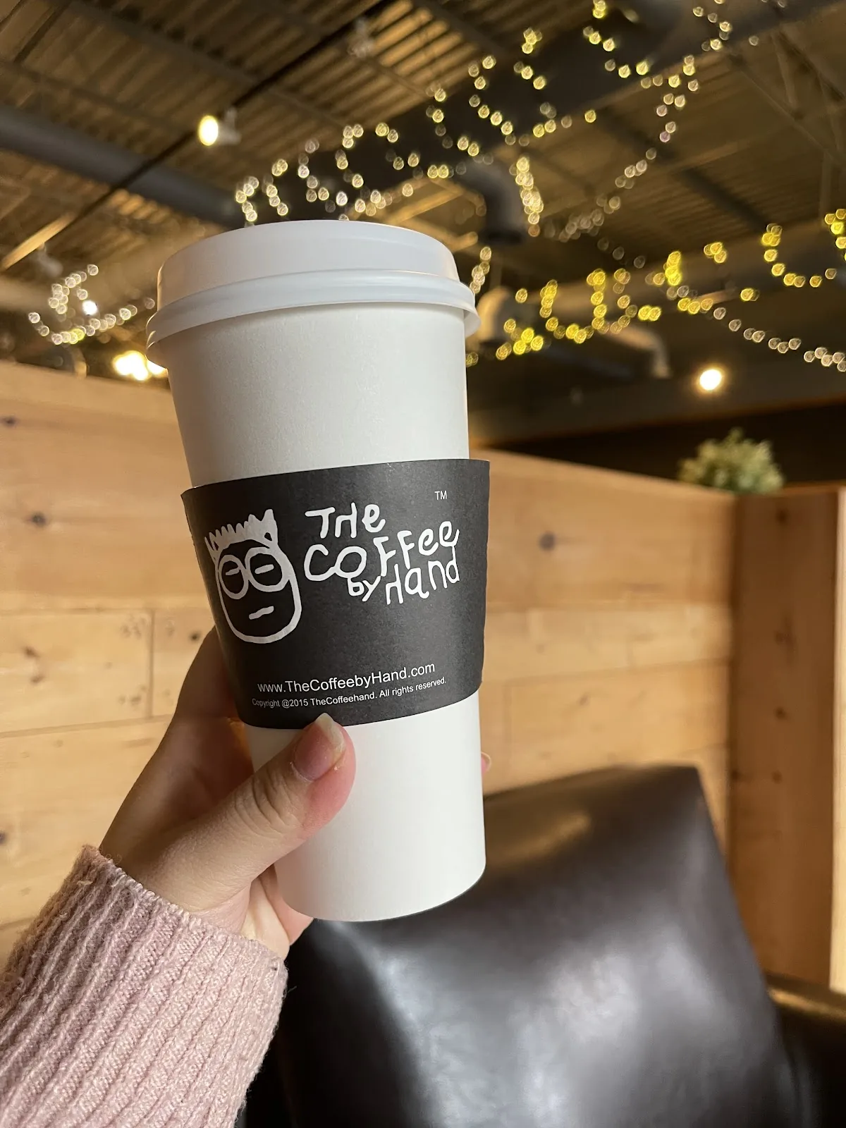A hand holding a branded takeaway cup outside the shop.